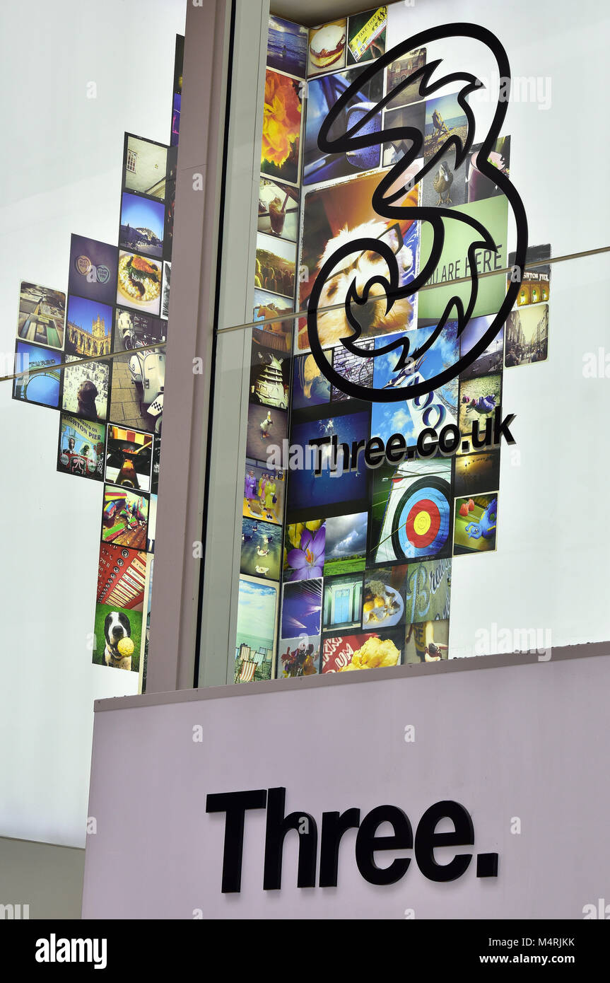 L'emblème d'un insigne ou logo de marque du téléphone mobile ou appareil portable géant des communications trois mobile 3. La publicité dans une fenêtre sur la th night street. Banque D'Images