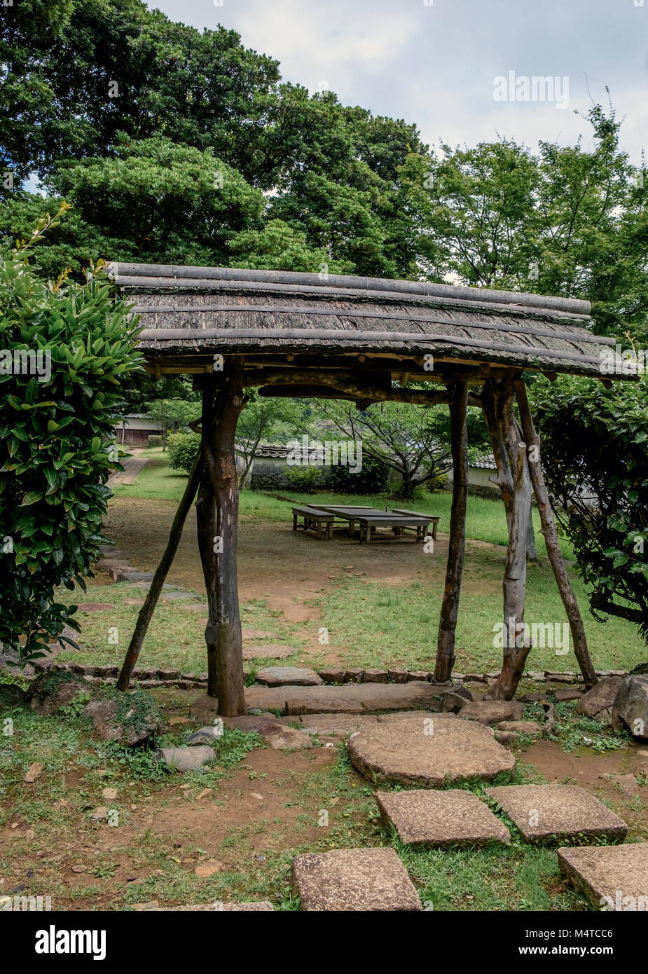 Au jardin du Musée Historique Matsura, Hirado, Nagasaki, Japon. Structure rustique avec toit dans le centre en bois rustique, table et chaises en arrière-plan. Banque D'Images