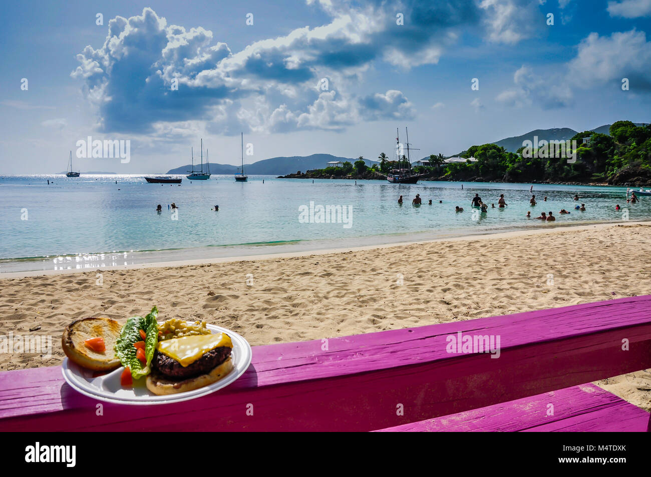 Assiette de cheeseburger et à salade sur banc fuschia rose sur la plage, l'île de miel de l'eau, des îles Vierges américaines. Banque D'Images