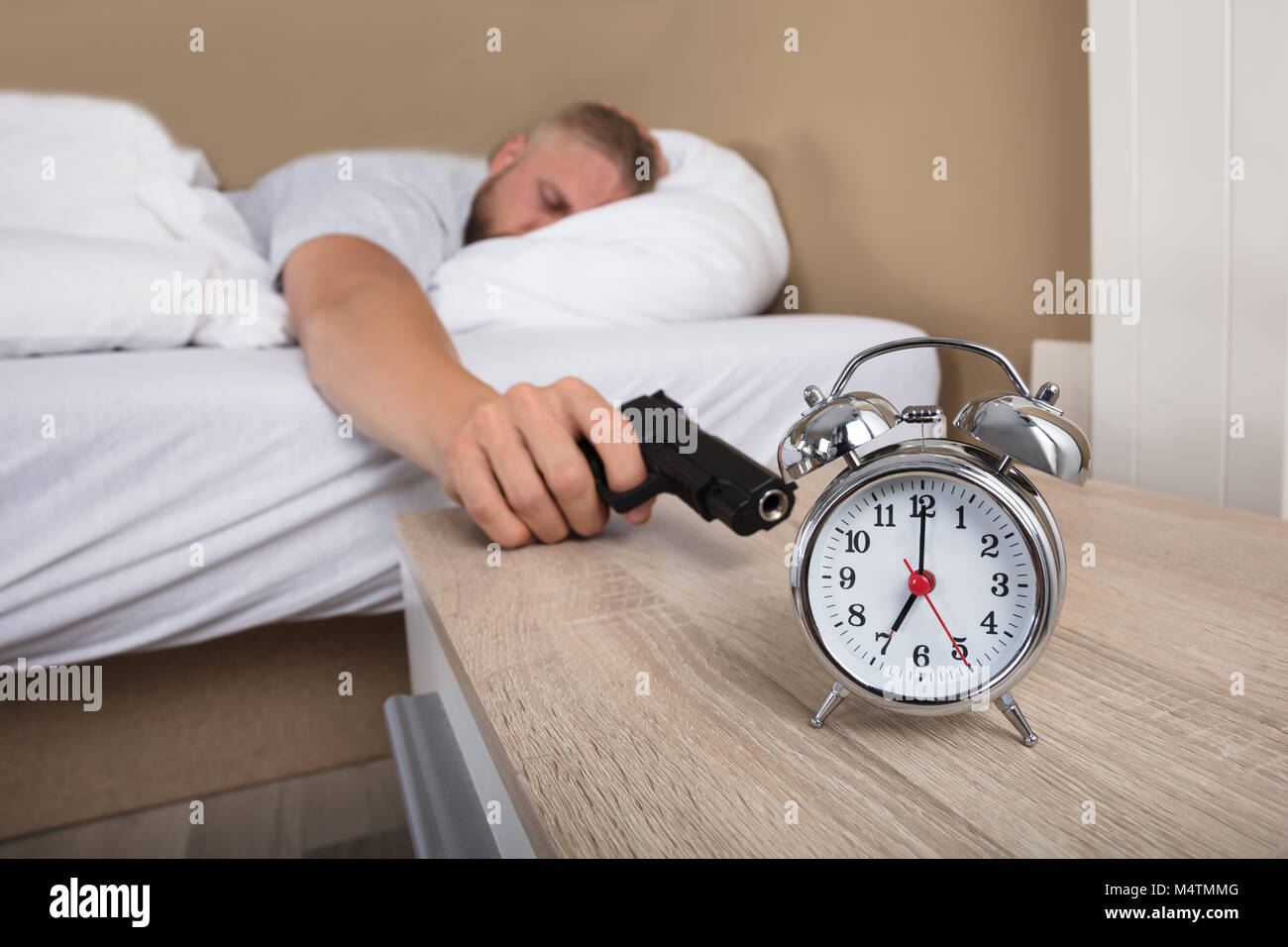 Young Man Lying On Bed Holding arme pour tirer Réveil Banque D'Images