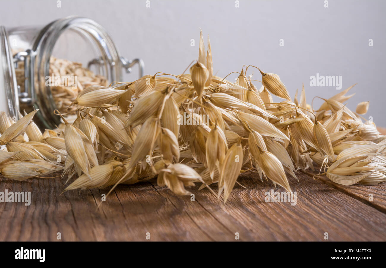 Close-up de grains d'avoine sur vintage table en bois. Le maïs mûr magnifique avec un bocal en verre rempli de flocons d'avoine dans l'arrière-plan. Faible profondeur de la netteté. Banque D'Images