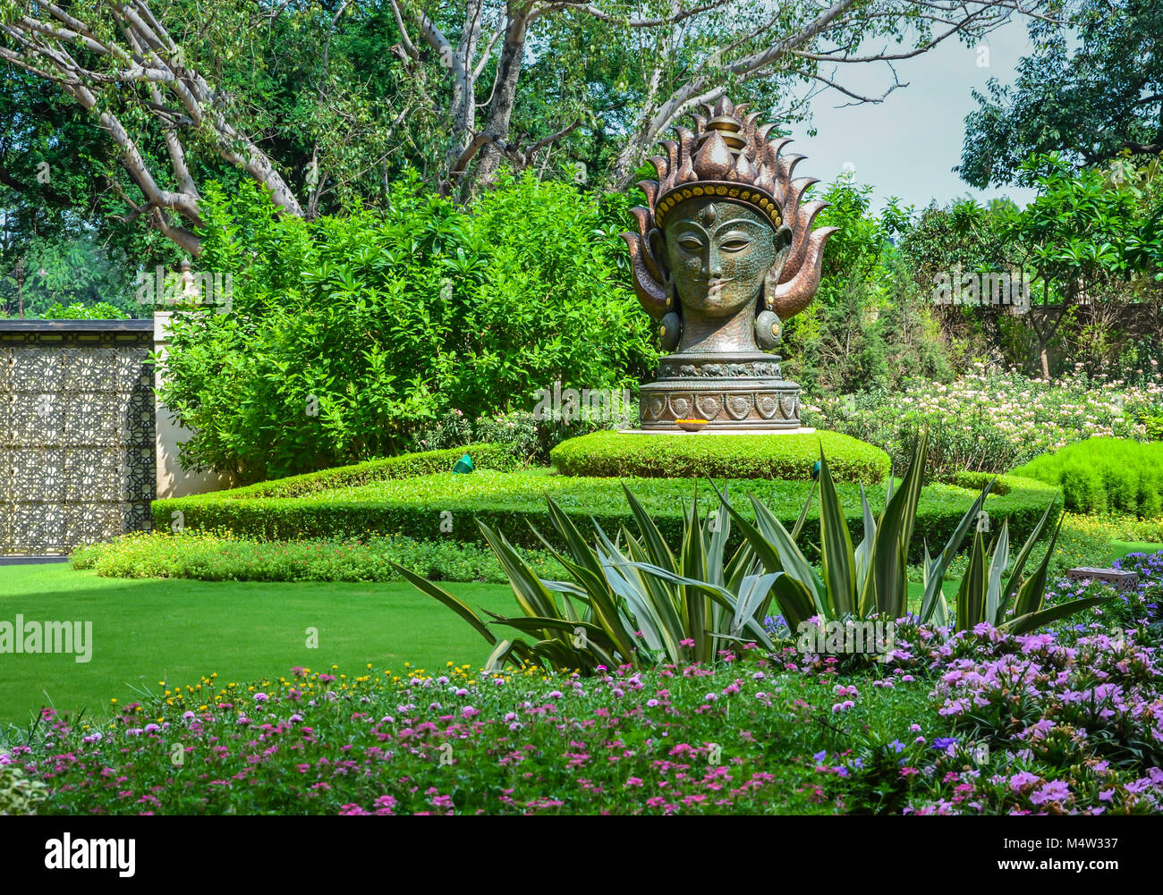 Jardin avec verdure subtile védique, varieted feuillage rayé violet, des annuelles, et une immense statue de la déesse de l'acier au Leela Palace, New Delhi, Inde. Banque D'Images