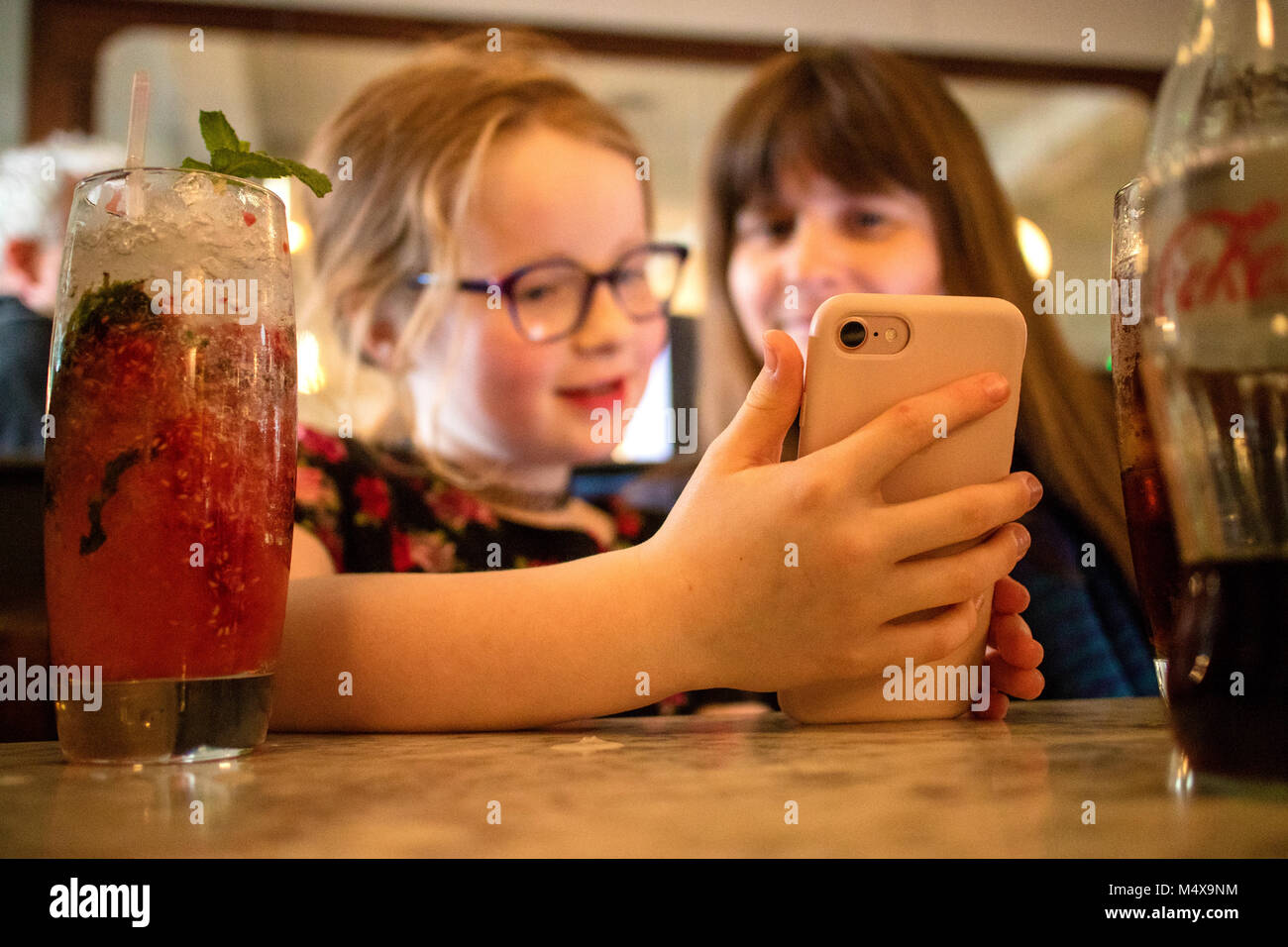 Mère et fille de 8 ans dans un bar très fréquenté et à jouer sur Apple iPhone Banque D'Images