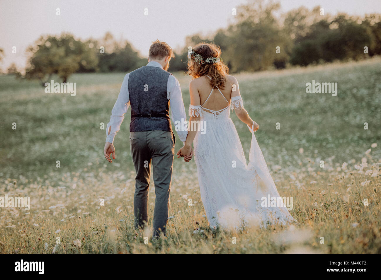 Belle jeune mariée et le marié à l'extérieur dans la nature verte au coucher de soleil romantique. Vue arrière. Banque D'Images