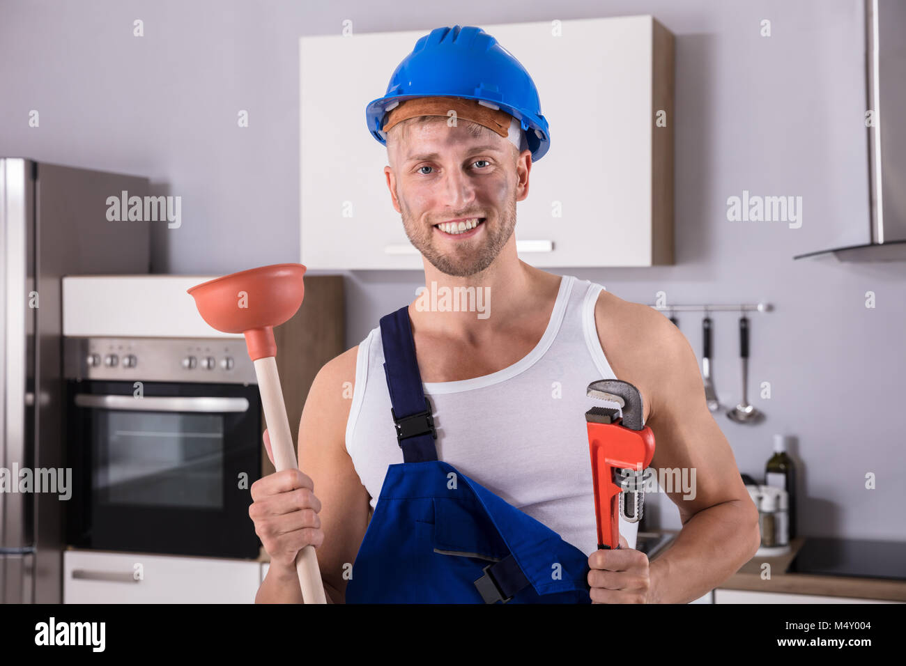 Portrait Of A Smiling Young clé de plombier et le plongeur dans la cuisine à la maison Banque D'Images