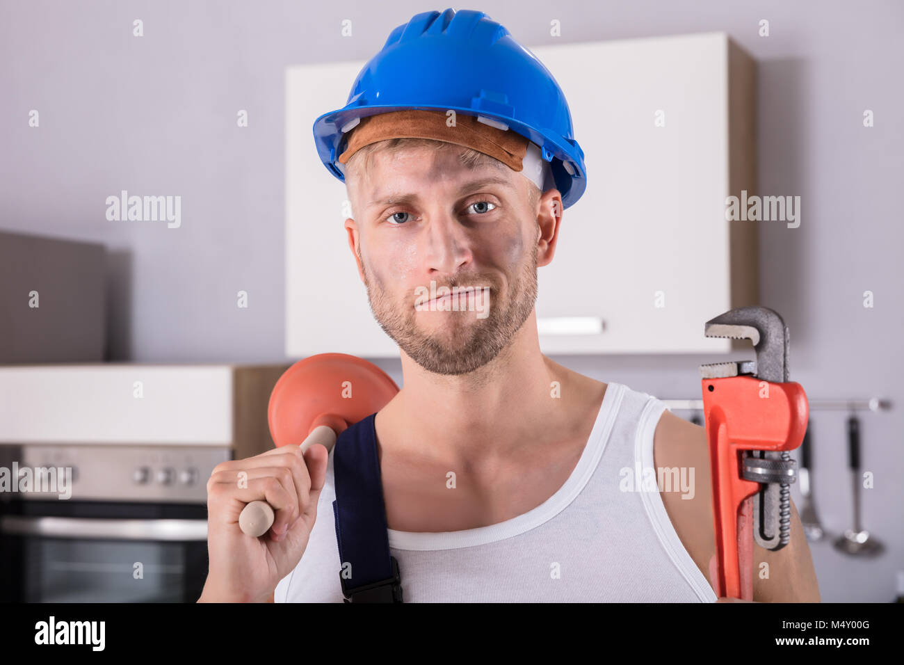 Portrait Of A Smiling Young clé de plombier et le plongeur dans la cuisine à la maison Banque D'Images