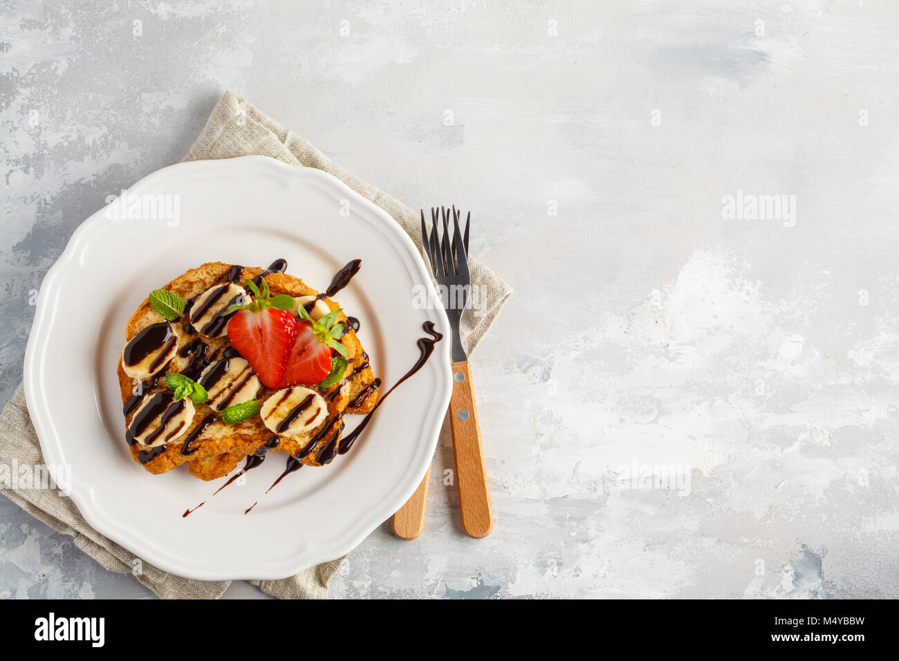 French toasts avec du sirop de chocolat, des fraises et une banane. Fond gris, copie espace, vue du dessus. Banque D'Images