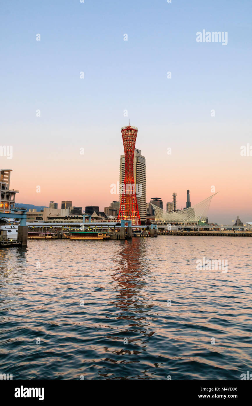 Le Japon, Kobe. Kobe port Tower, rouge avec l'Okura Hotel derrière, et le musée maritime sur le front de mer. Le crépuscule juste après le coucher du soleil, ciel orange au bleu. Banque D'Images