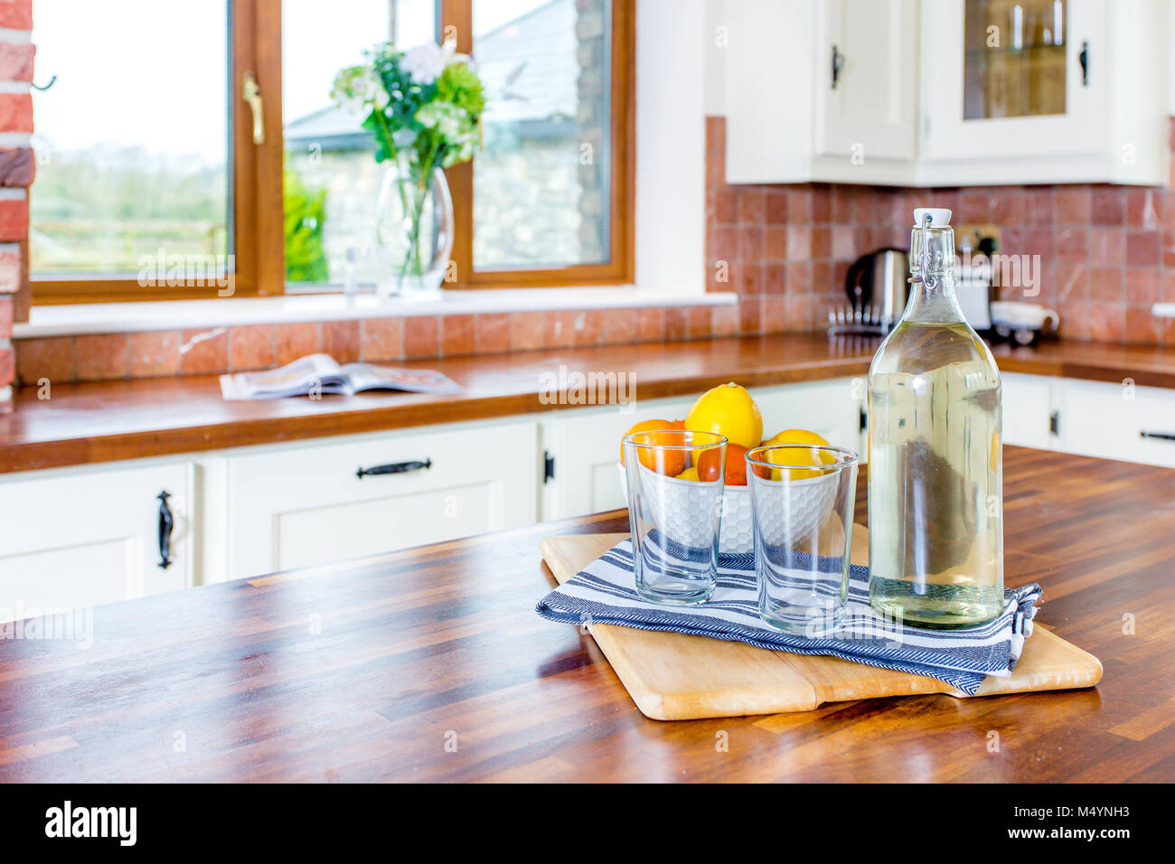 Cuisine intérieur avec décoration de table - bouteille d'eau en verre avec bouchon, bol de fruits et les verres, planche à découper en bois, serviette. Home staging. Banque D'Images