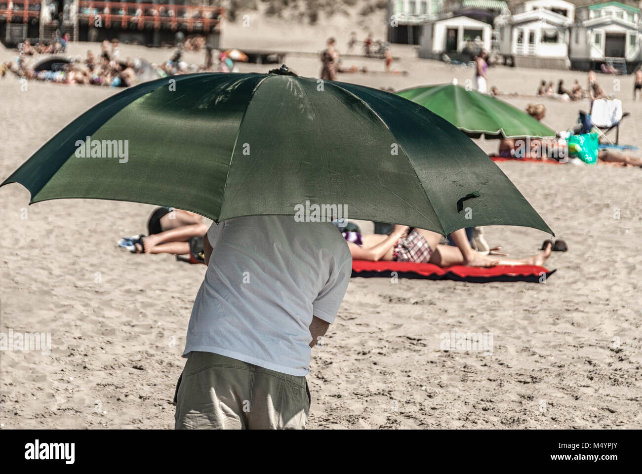 Homme marchant sur la plage sous un parapluie vert protégeant du soleil Banque D'Images