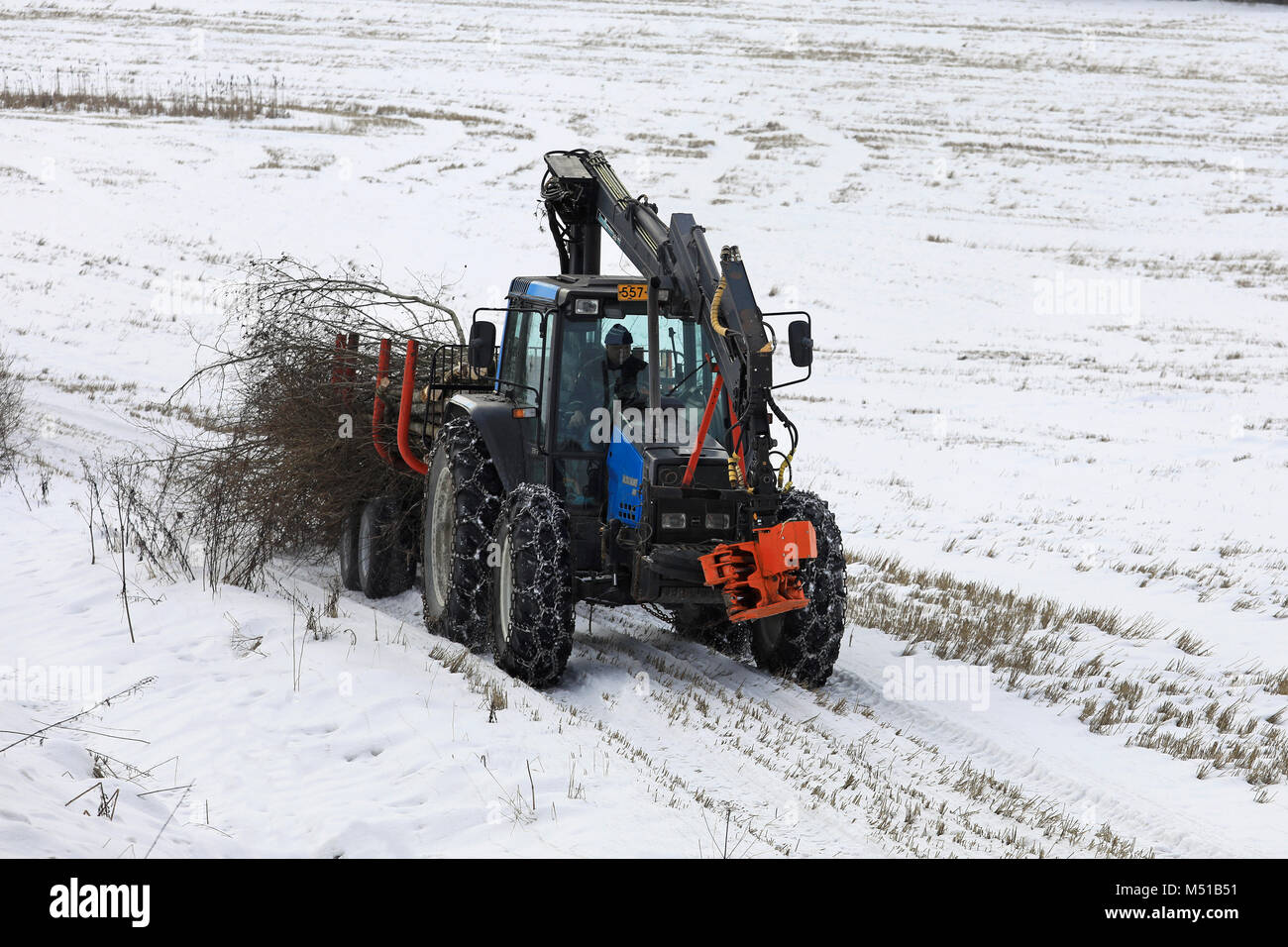 SALO, FINLANDE - le 16 février 2018 : agriculteur transporte une charge de broussailles avec Valmet Valtra tracteur et remorque forestière le long du côté d'un champ neigeux Banque D'Images