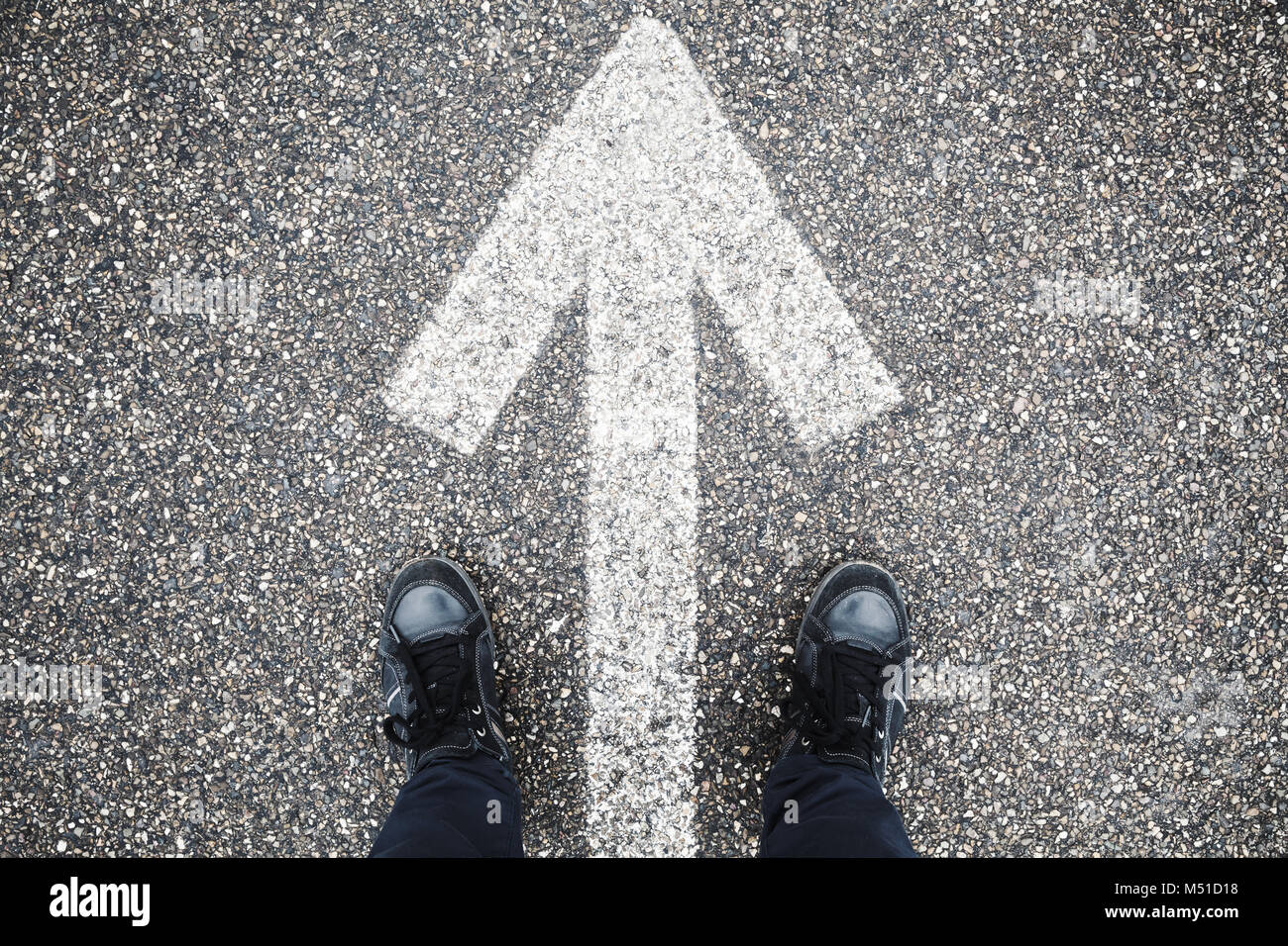 Les pieds mâles en jean bleu et des chaussures en cuir noir sur le stand d'asphalte de la rue avec une flèche blanche signalisation Banque D'Images