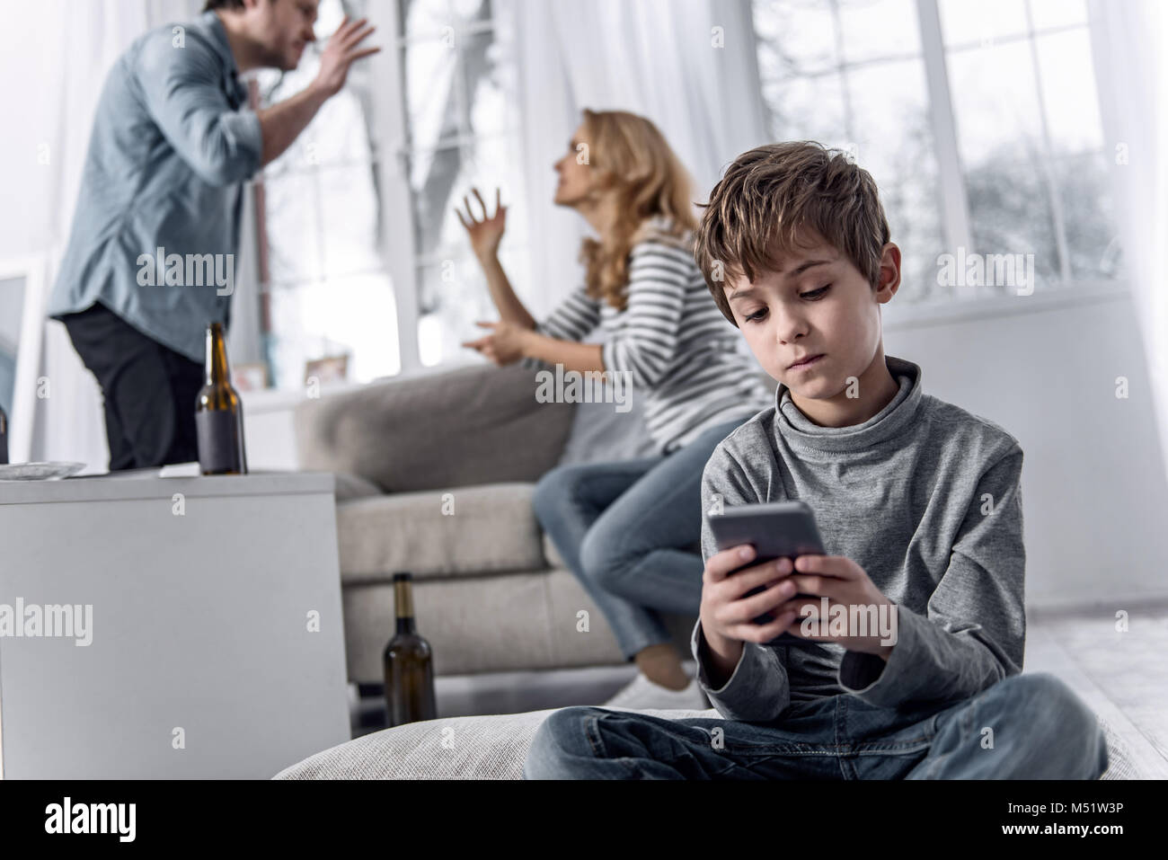 Garçon calme tenant un smartphone pendant que ses parents ayant une voix forte querelle Banque D'Images