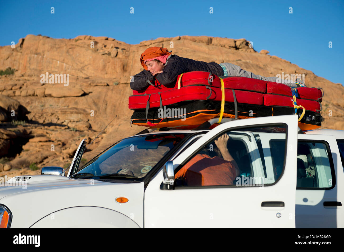 Woman sleeping on crash pad en haut de voiture pendant bouldering expedition, Spitzkoppe, région d'Erongo, Namibie Banque D'Images