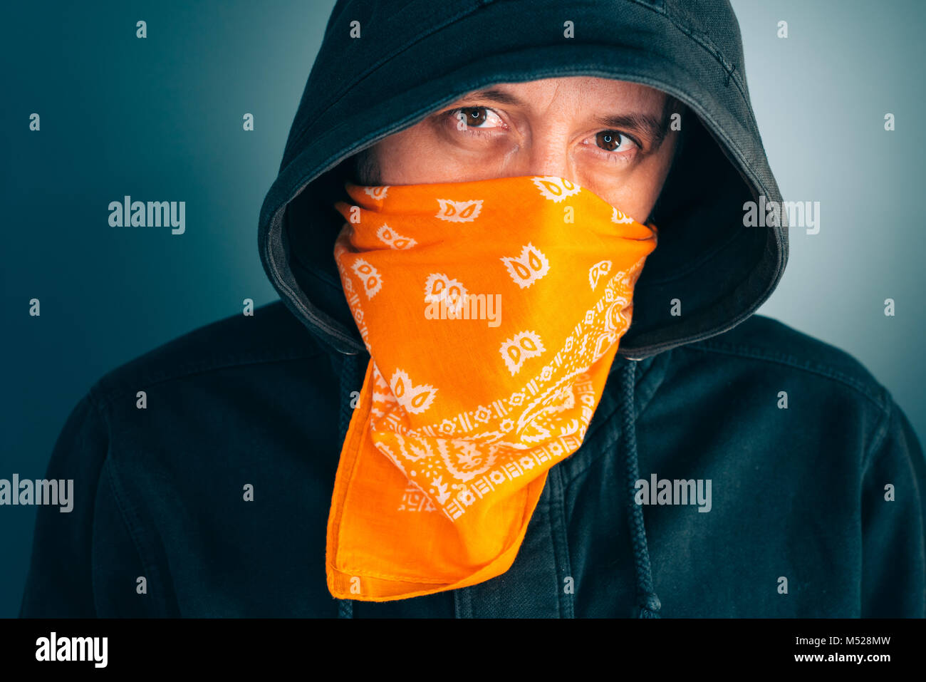 Portrait de l'homme criminel masqué looking at camera. Homme adulte avec capuche et écharpe sur le visage comme bandit ou membre d'un gang. Banque D'Images