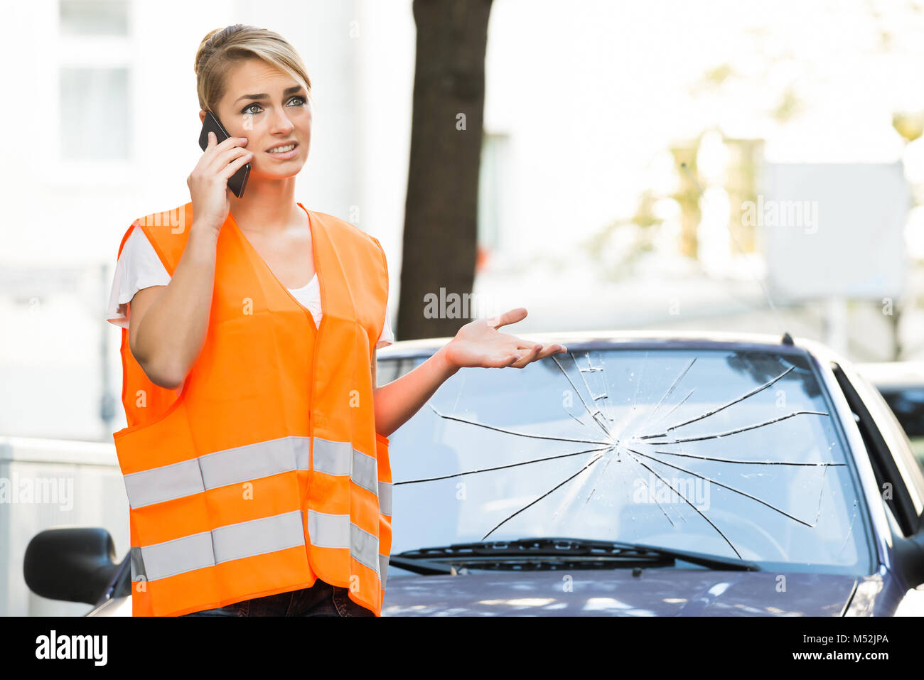 Femme en veste réfléchissante Talking On Mobile Phone In front of Broken Glass de voiture Banque D'Images