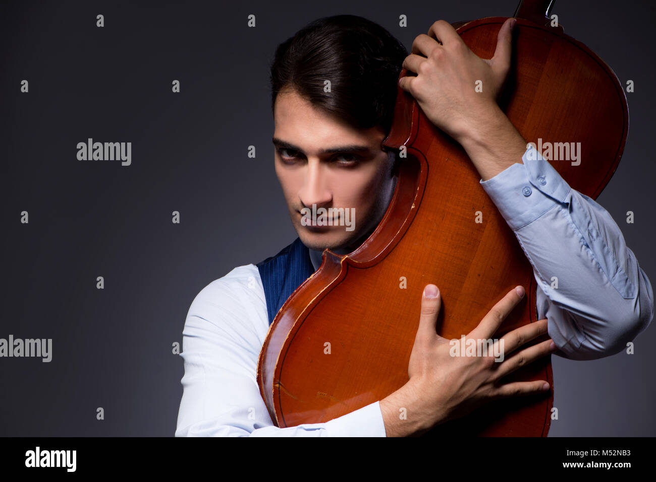 Jeune homme jouant du violoncelle in dark room Banque D'Images