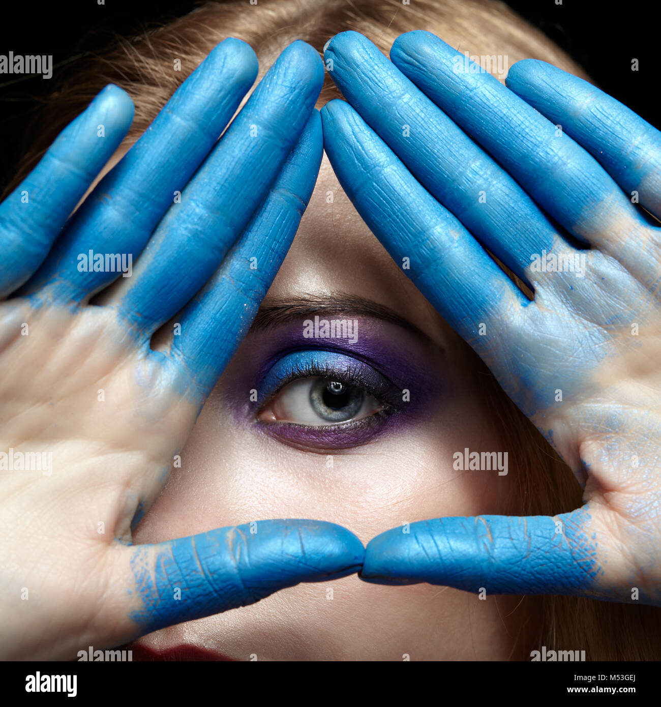 L'œil de la Providence, symbole de l'œil de pyramide mains et visage de femme avec peinture bleu sur les doigts Banque D'Images