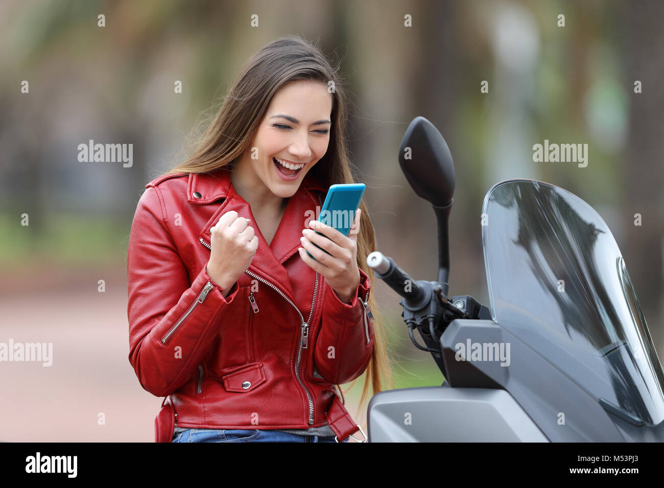 Motorbiker excité sur une moto lecture bonnes nouvelles en ligne dans un téléphone intelligent Banque D'Images