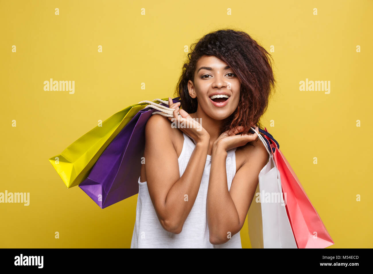Shopping Concept - Portrait de Portrait young African woman smiling belle attrayante et joyeuse avec sac shopping coloré. Pastel jaune fond mur. Copier l'espace. Banque D'Images