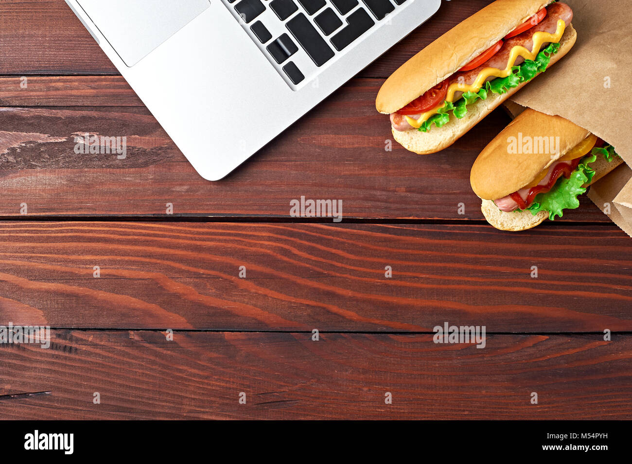 Déjeuner d'affaires dans l'espace de bureau, vue de dessus de Hot Dog sur un bureau en bois près de l'ordinateur portable Clavier d'ordinateur. Mise à plat. Restauration rapide livraison. Banque D'Images