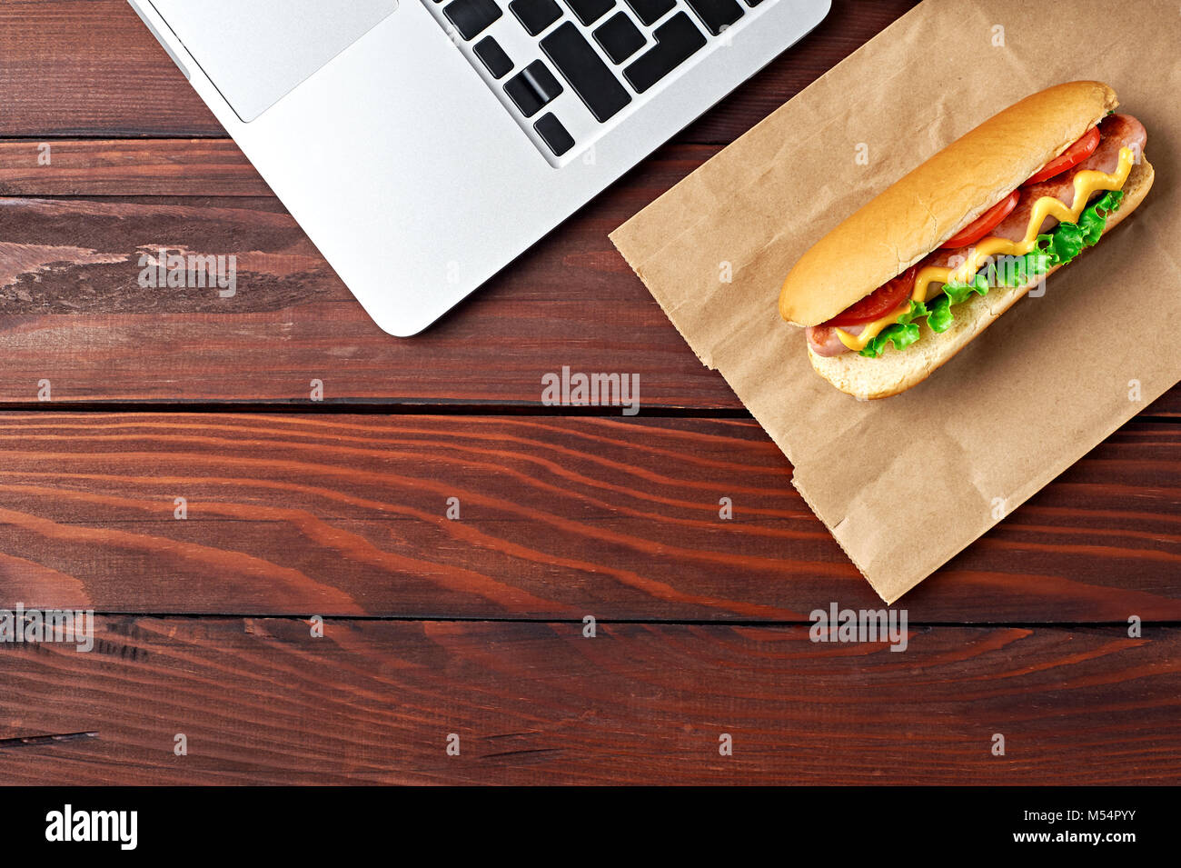 Déjeuner d'affaires dans l'espace de bureau, vue de dessus de Hot Dog sur un bureau en bois près de l'ordinateur portable Clavier d'ordinateur. Mise à plat. Restauration rapide livraison. Banque D'Images