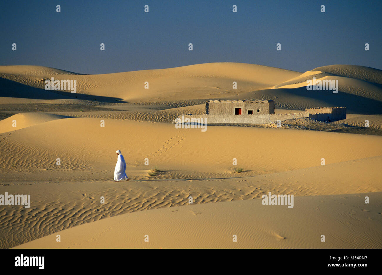 L'Algérie. Près de Touggourt. La Mer de Sable. Grand Erg Oriental. Désert du Sahara. Maisons traditionnelles en oasis. Bedouin man walking. Banque D'Images