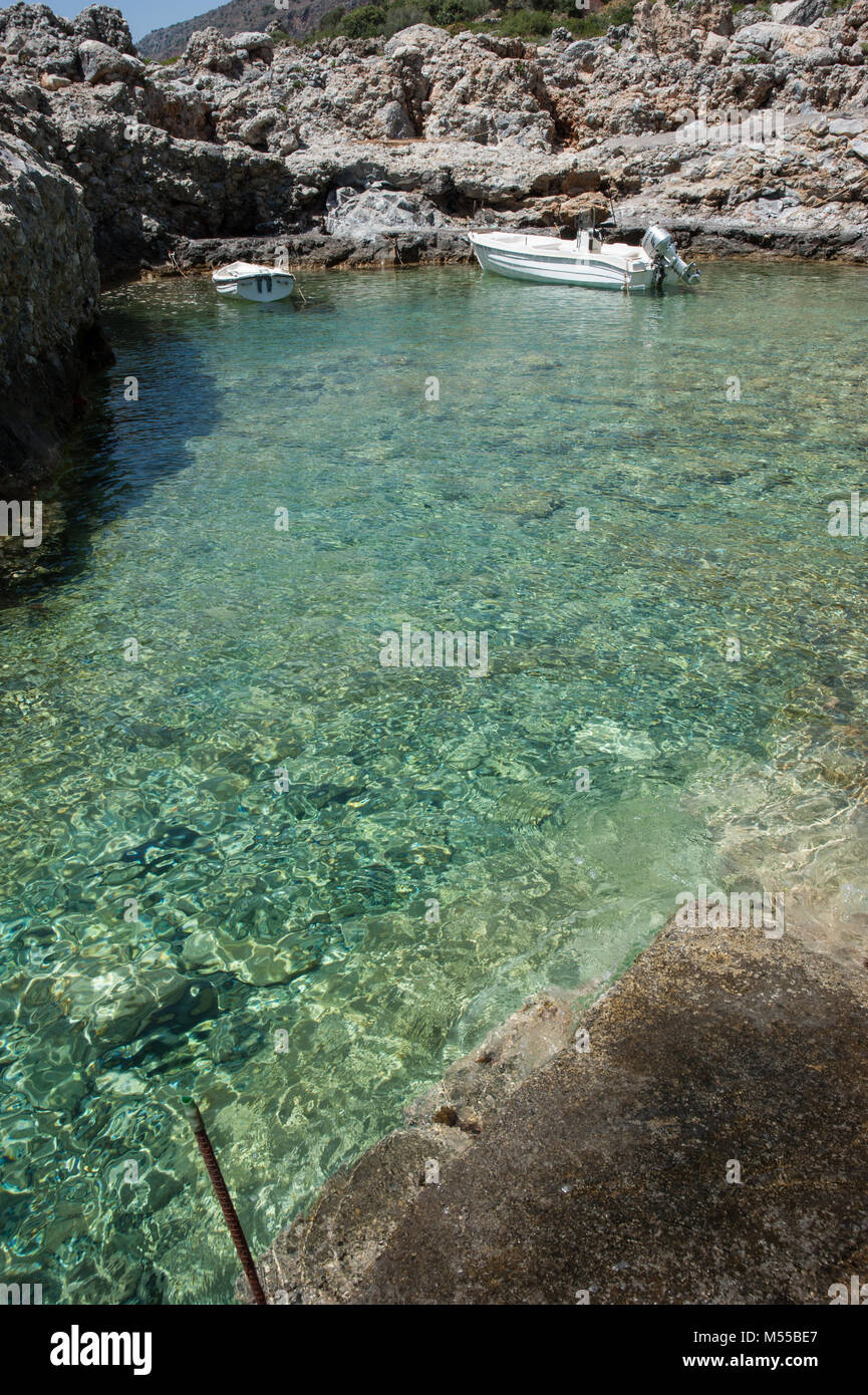 Les eaux vert émeraude scintillant sur un rivage rocailleux avec deux bateaux à moteur dans le Péloponnèse, Grèce. Banque D'Images