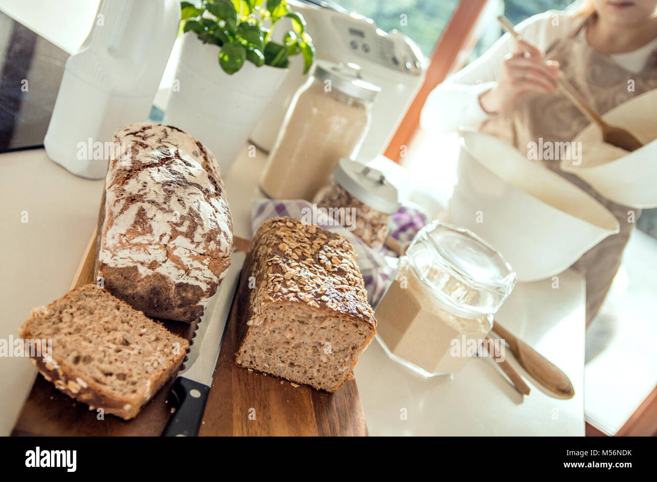 Pain maison saine allongé sur un comptoir. Femme prépare une autre pâte en arrière-plan. Photo prise à la lumière de soleil naturel et studio lampes. Il Banque D'Images