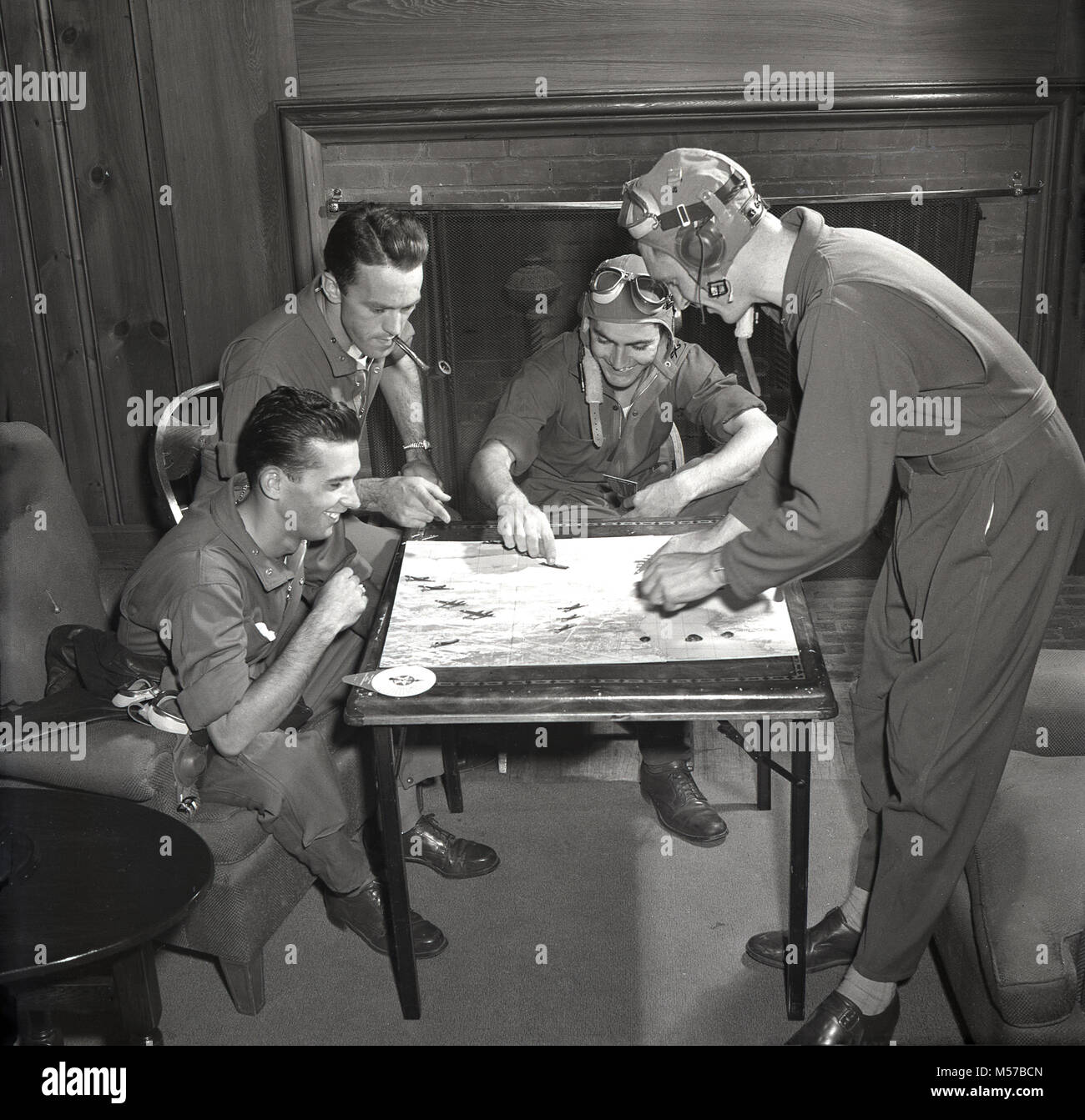 1942, USA, historique, quatre militaires de l'United States Army Air Forces (USAAF) portent leur kit de vol assis dans un salon de jouer le nouveau jeu de combat aérien, 'Trainer'. Produite en collaboration avec le ministère de la guerre des États-Unis, le jeu est un test de compétence de vol de combat à l'aide de miniatures d'avions de guerre et de combat. Banque D'Images