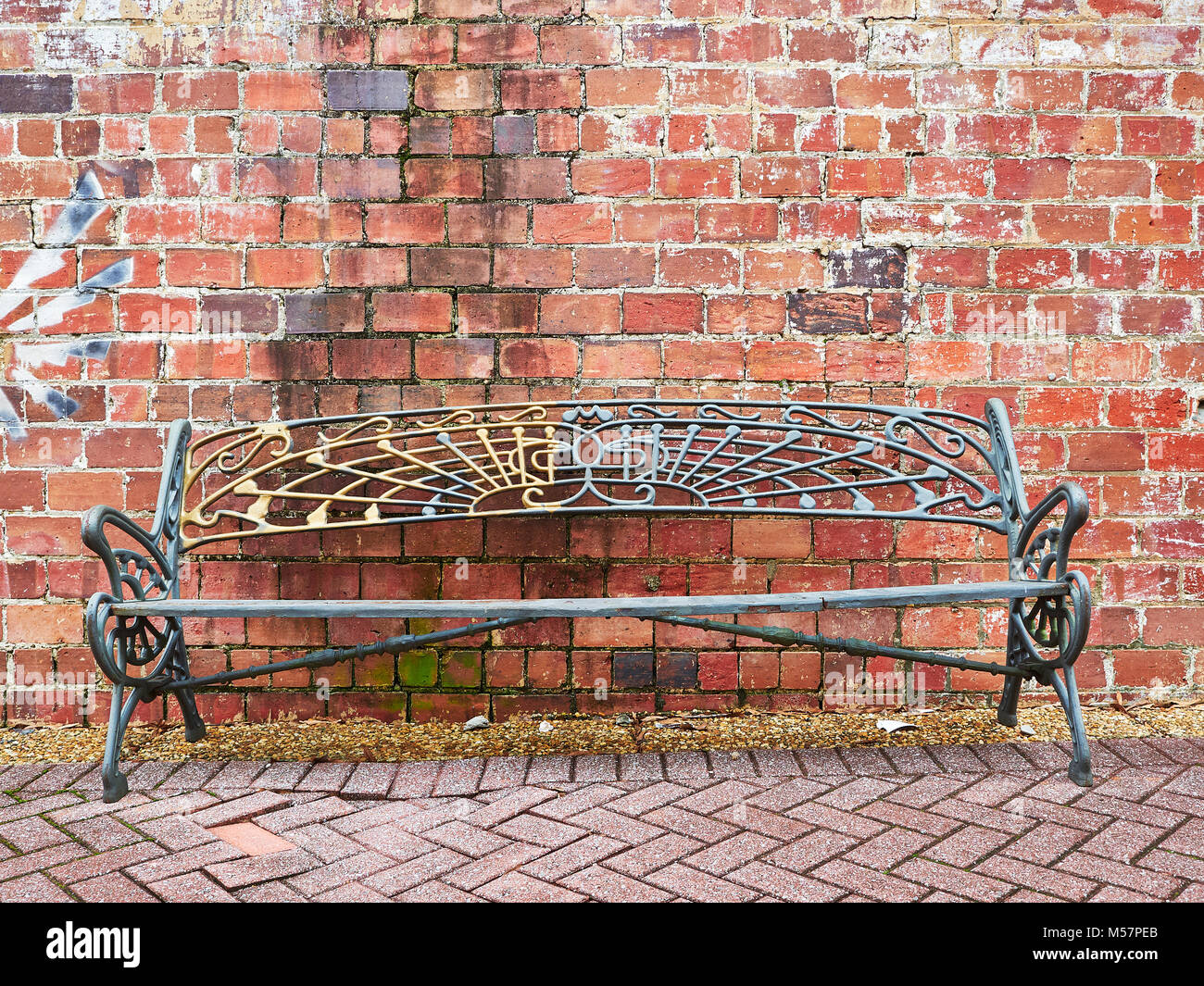 Simple fer metal banc de parc inoccupé contre un vieux mur de briques paves en face. Banque D'Images