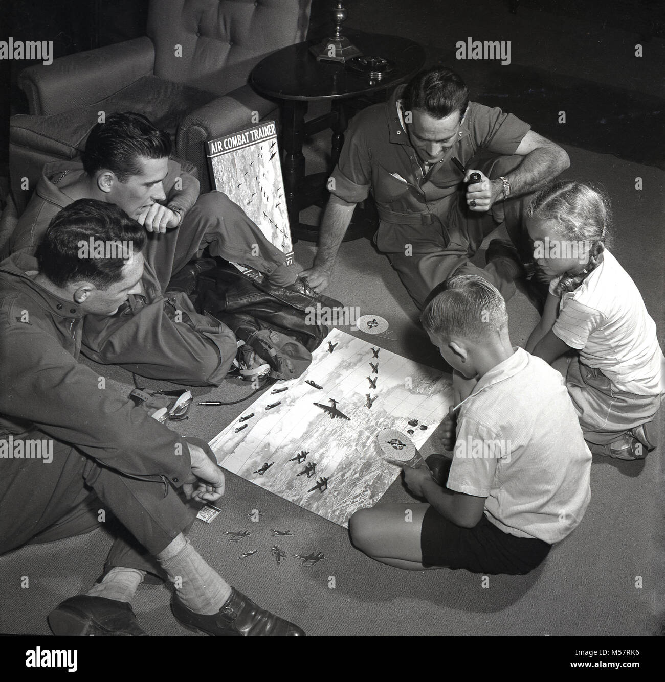 1942, USA, historique, trois militaires de l'United States Army Air Forces (USAAF) portent leur kit de vol assis à l'intérieur de jouer le nouveau jeu de combat aérien, 'Trainer' avec deux jeunes enfants. Produite en collaboration avec le ministère de la guerre des États-Unis, le jeu est un test de compétence de vol de combat à l'aide de miniatures d'avions de guerre et de combat. Banque D'Images