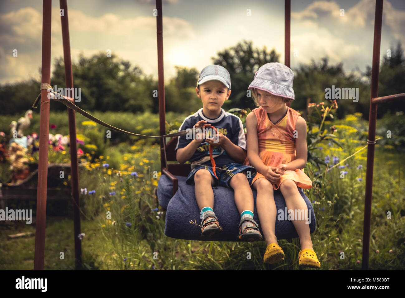Les enfants garçon et fille se balançant ensemble en journée d'été sur l'arrière-cour en campagne enfance heureux concept Banque D'Images