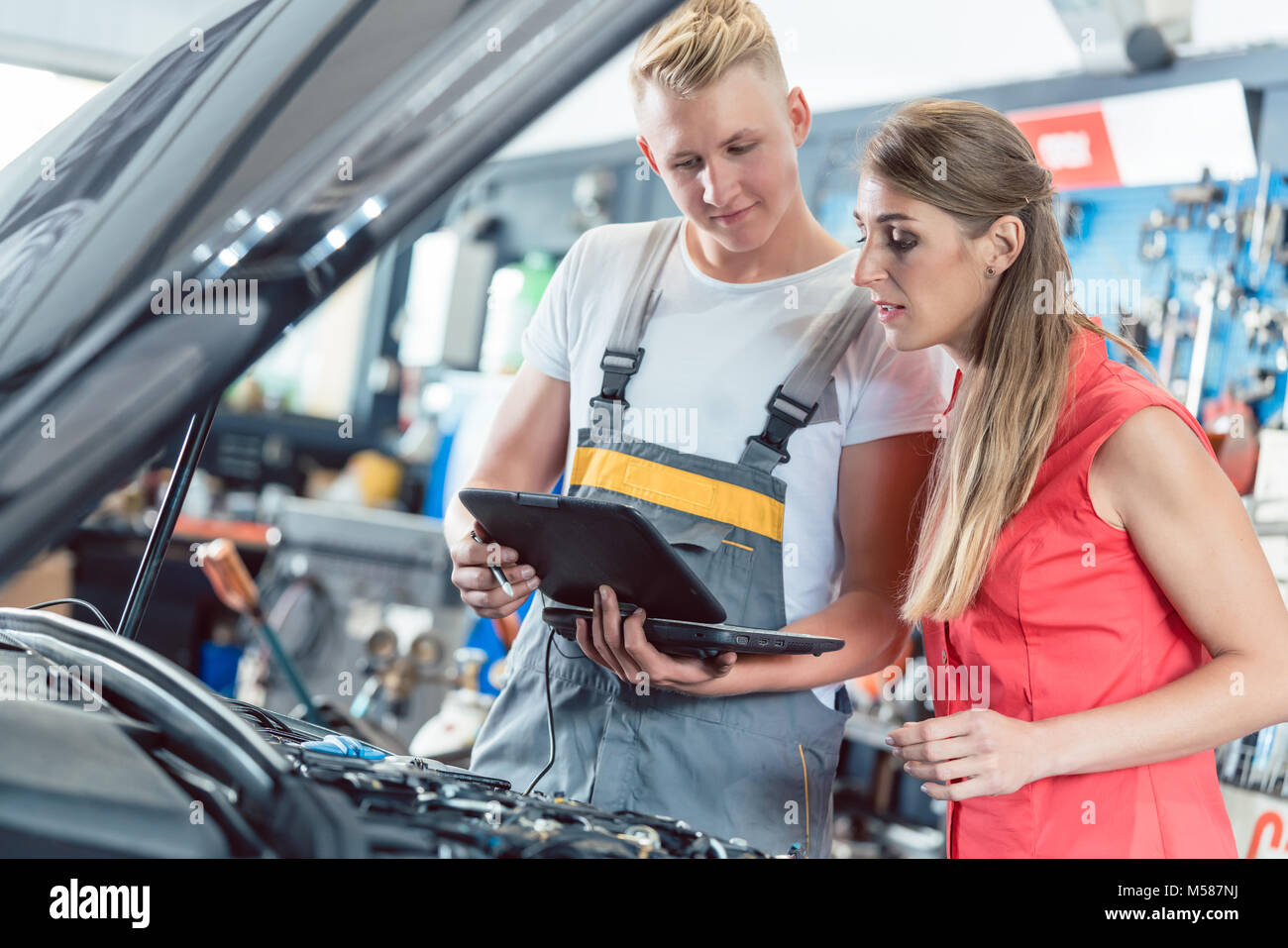 Mécanicien auto fiable montrant à un client femelle les codes d'erreur de moteur scanné par un logiciel de diagnostic de voiture dans un atelier de réparation automobile moderne Banque D'Images