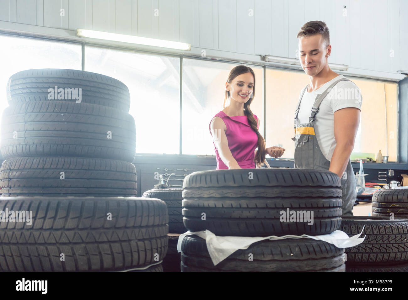 Belle auto mechanic aide une clientèle féminine de choisir entre différents pneus de haute qualité dans un atelier de réparation automobile contemporaine Banque D'Images