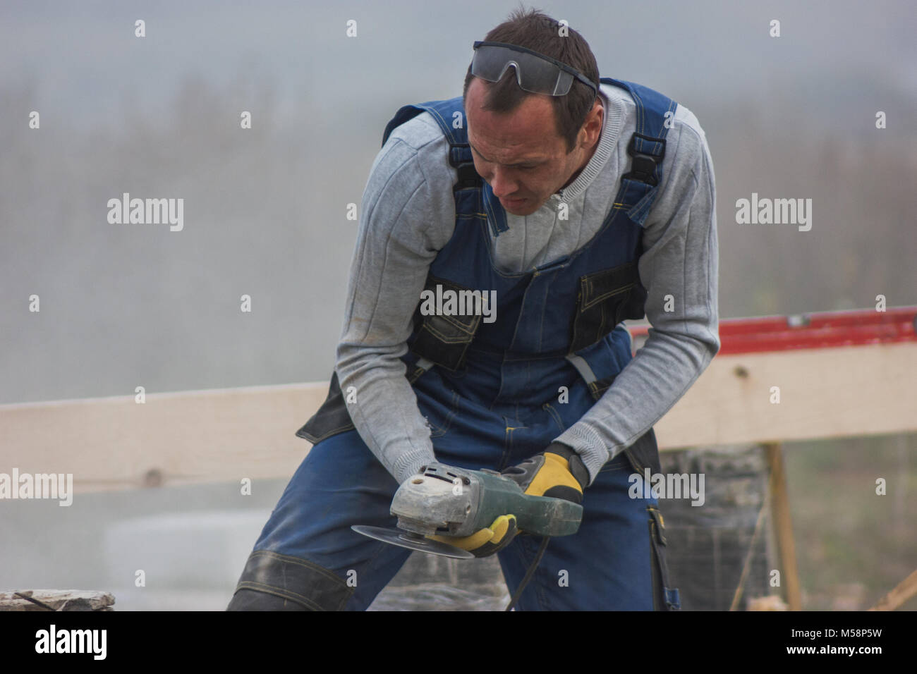 L'homme travailleur builder travailler avec une scie circulaire à l'extérieur, volant autour de la sciure Banque D'Images