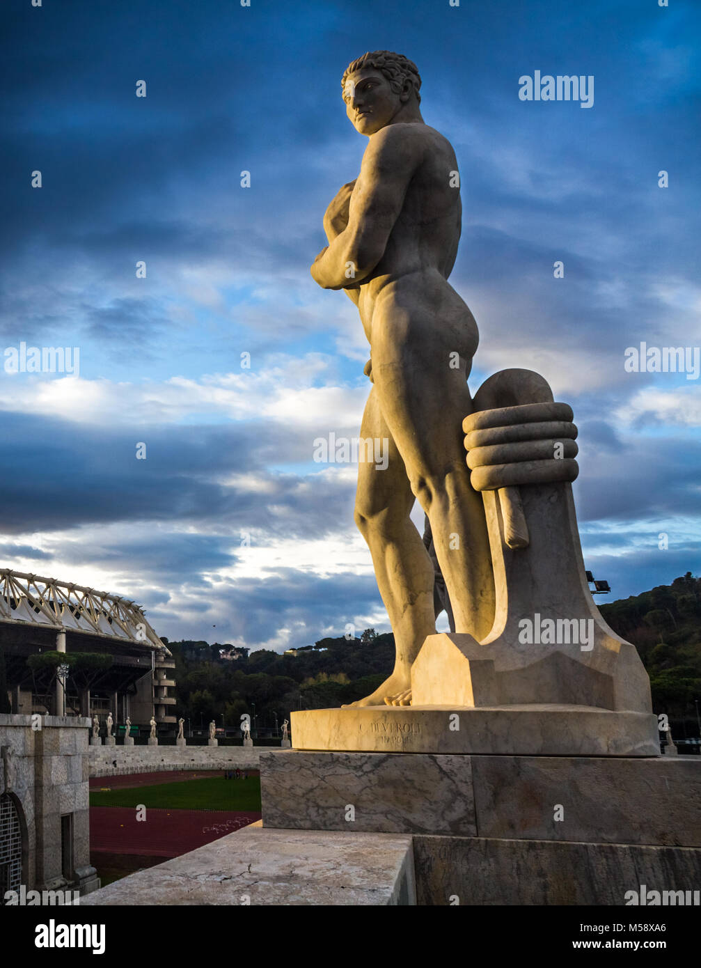 Des statues représentant des athlètes au Stadio dei Marmi à Rome. Dans l'arrière vous pouvez voir le stade olympique. La scène est éclairée par la lumière et le coucher du soleil spectaculaire Banque D'Images