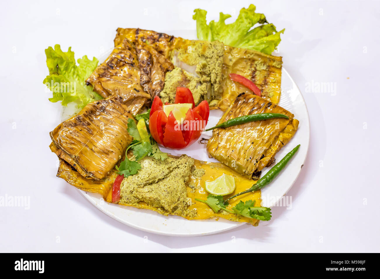Au four épicées de la cuisine indienne de poisson connu sous le Bhetki Paturi garnie avec feuille de chou tomate et piment vert. Banque D'Images