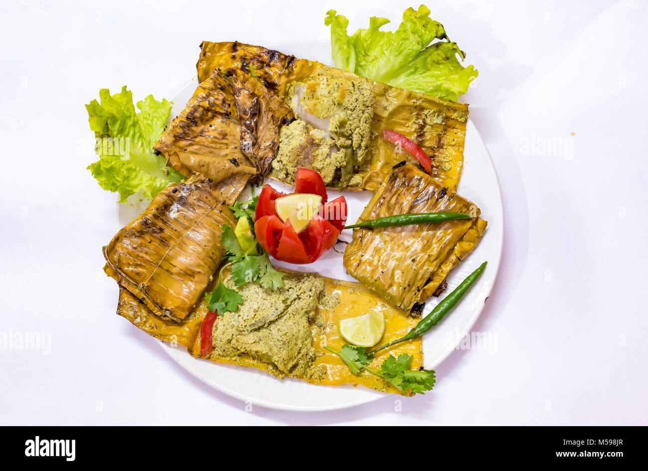 Au four épicées de la cuisine indienne de poisson connu sous le Bhetki Paturi garnie avec feuille de chou tomate et piment vert. Banque D'Images