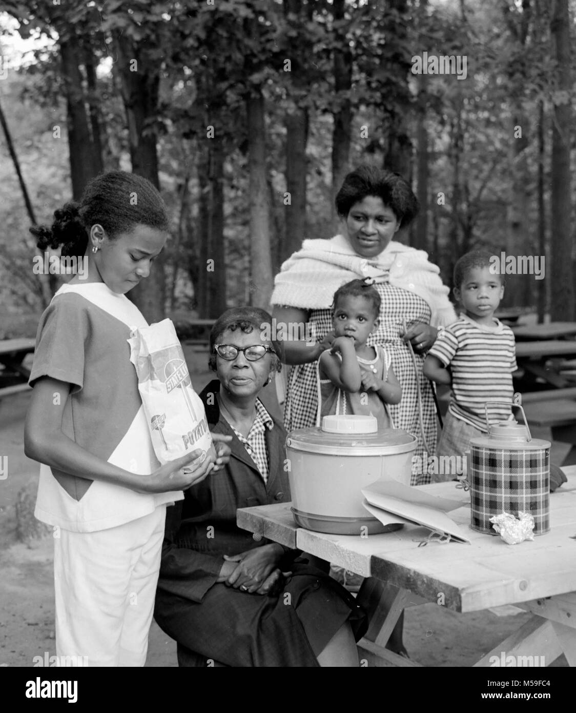 Une famille afro-américaine s'apprête à prendre un sac de la région de croustilles de pommes de terre à un banc de pique-nique en Nouvelle Angleterre, ca. 1958. Banque D'Images