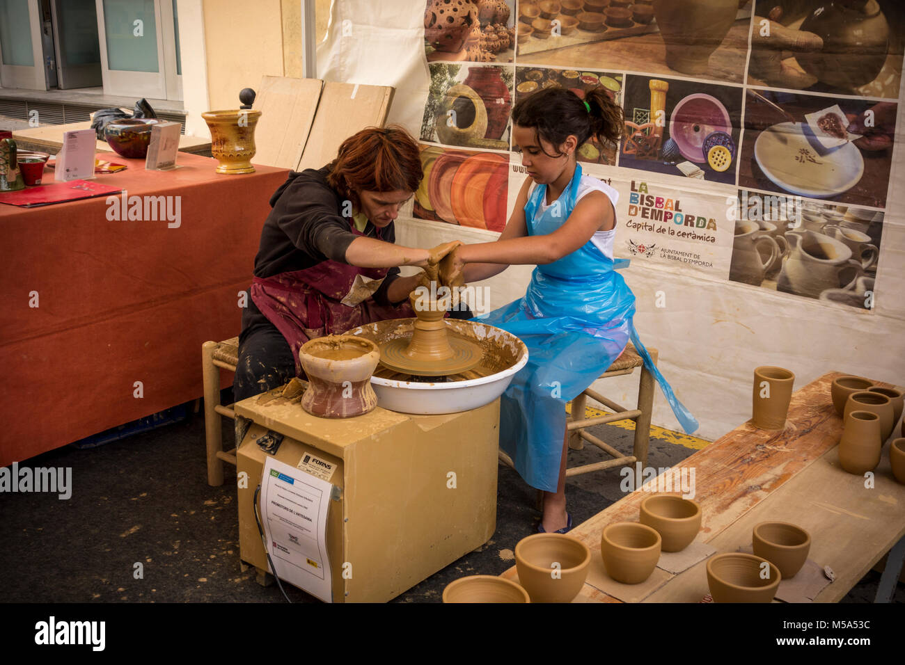 Une femelle potter aider les jeunes fille pour faire pot en argile sur la roue de fortune en flexion au marché hebdomadaire de l'atelier de céramique de La Bisbal d'Emporda, Baix Empor Banque D'Images