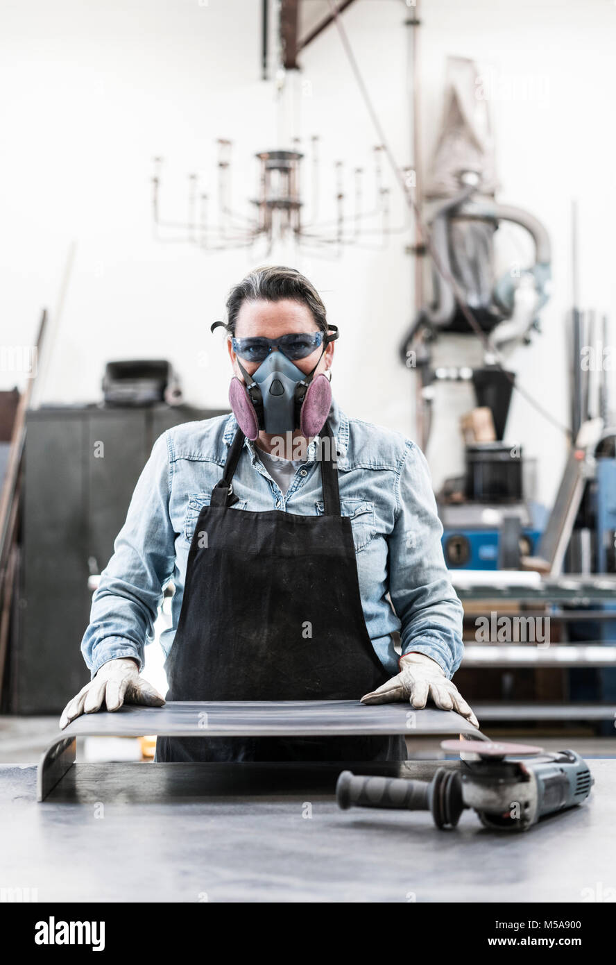 Femme portant des lunettes et masque antipoussière, debout dans l'atelier de métal, looking at camera. Banque D'Images