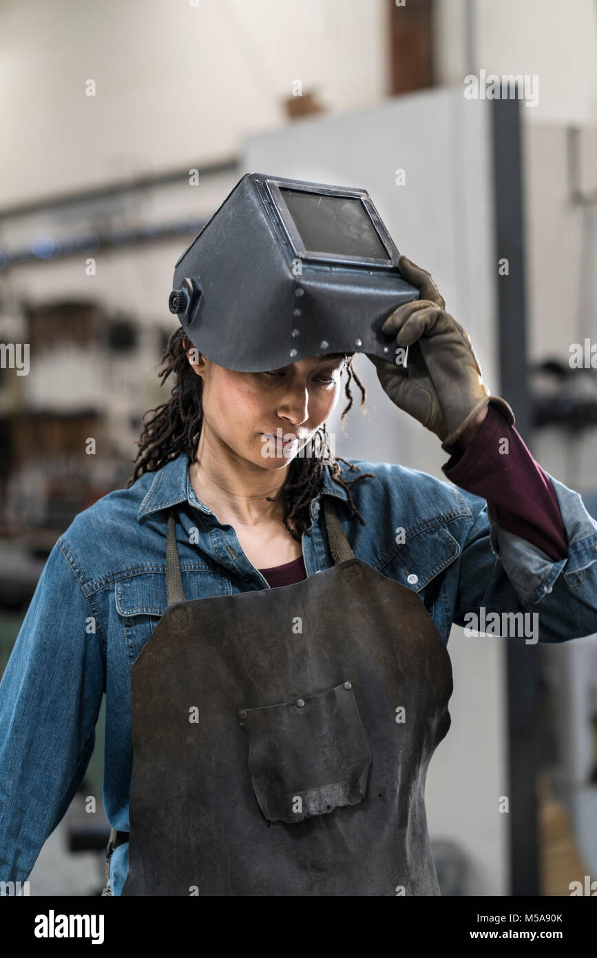 Portrait of woman wearing apron et masque de soudage debout dans l'atelier de métal. Banque D'Images