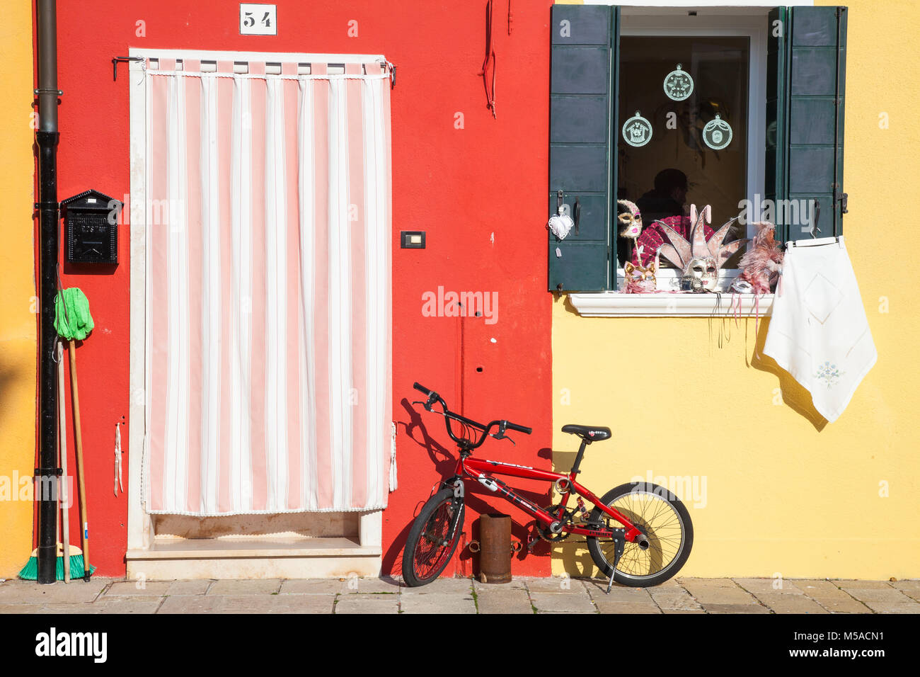 L'île de Burano, Venise, Vénétie, Italie. Jaune et rouge vif avec une location maisons et fenêtre habillé pour le carnaval avec des masques Banque D'Images