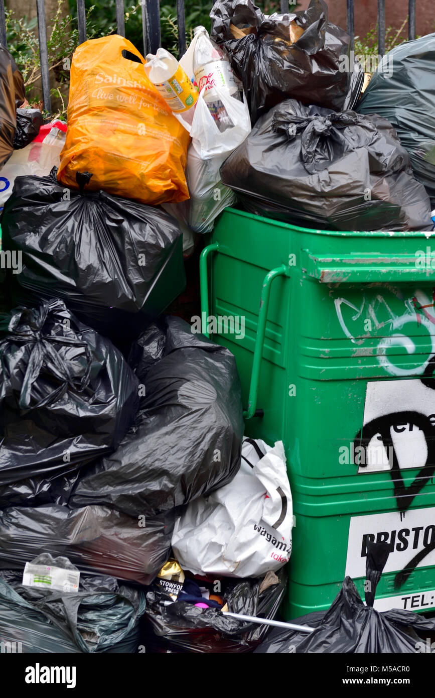 Déchets et ordures ménagères dans des sacs poubelle noirs empilés à côté de poubelle débordants, UK Banque D'Images