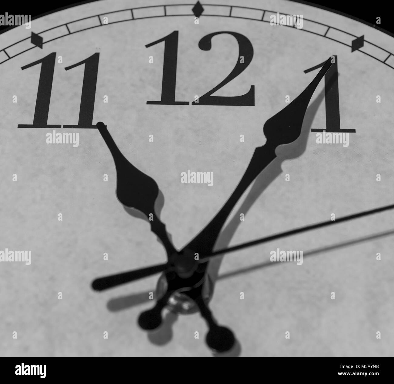 Gros plan sur les pointeurs d'une horloge marquant cinq minutes après 11 heures - le rendu noir et blanc Banque D'Images