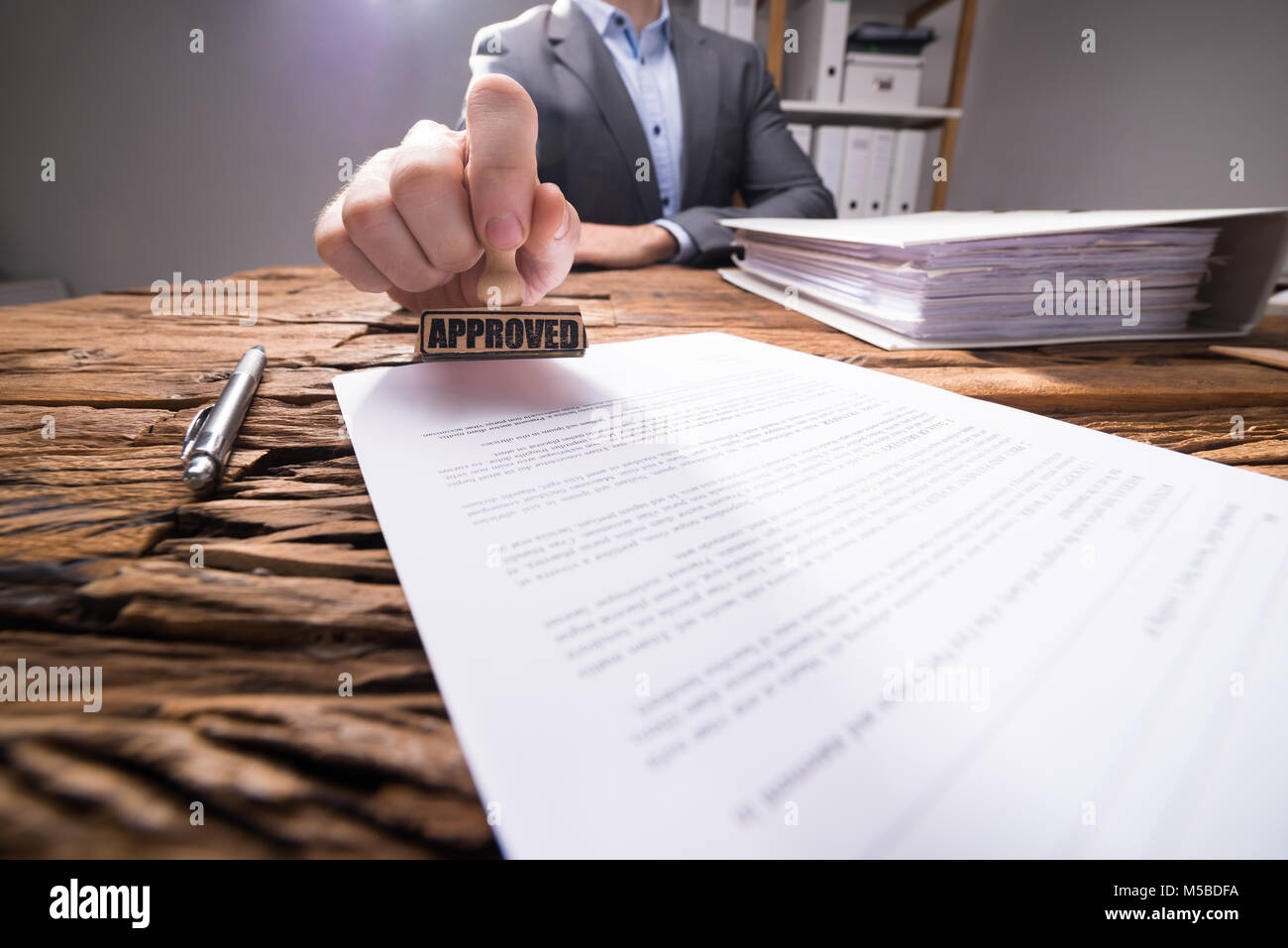Close-up de l'homme d'affaires à l'aide de Stamper sur le document avec le texte approuvé au bureau en bois Banque D'Images