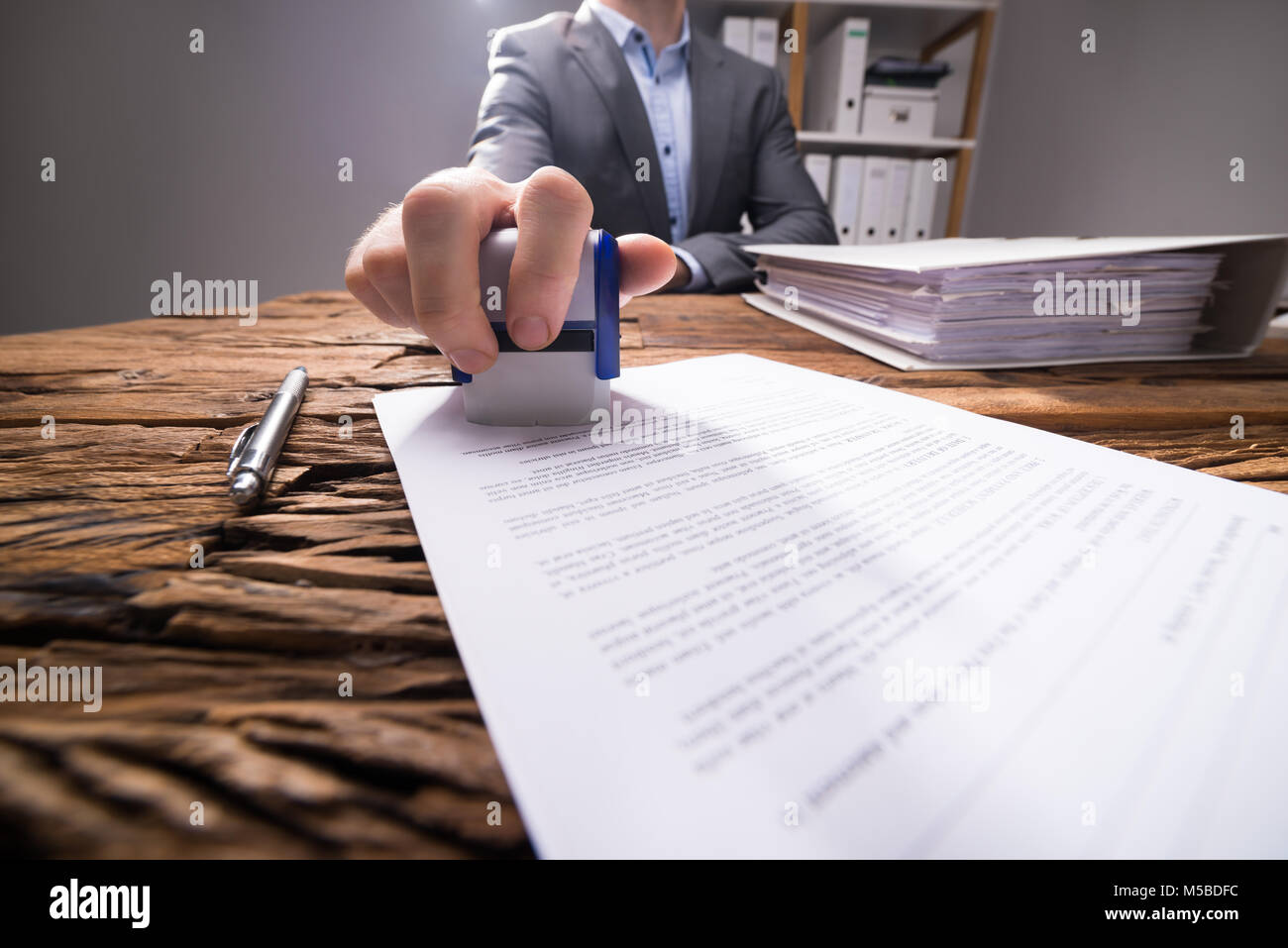 Close-up de l'homme d'affaires à l'aide de Stamper sur le document avec le texte approuvé au bureau en bois Banque D'Images