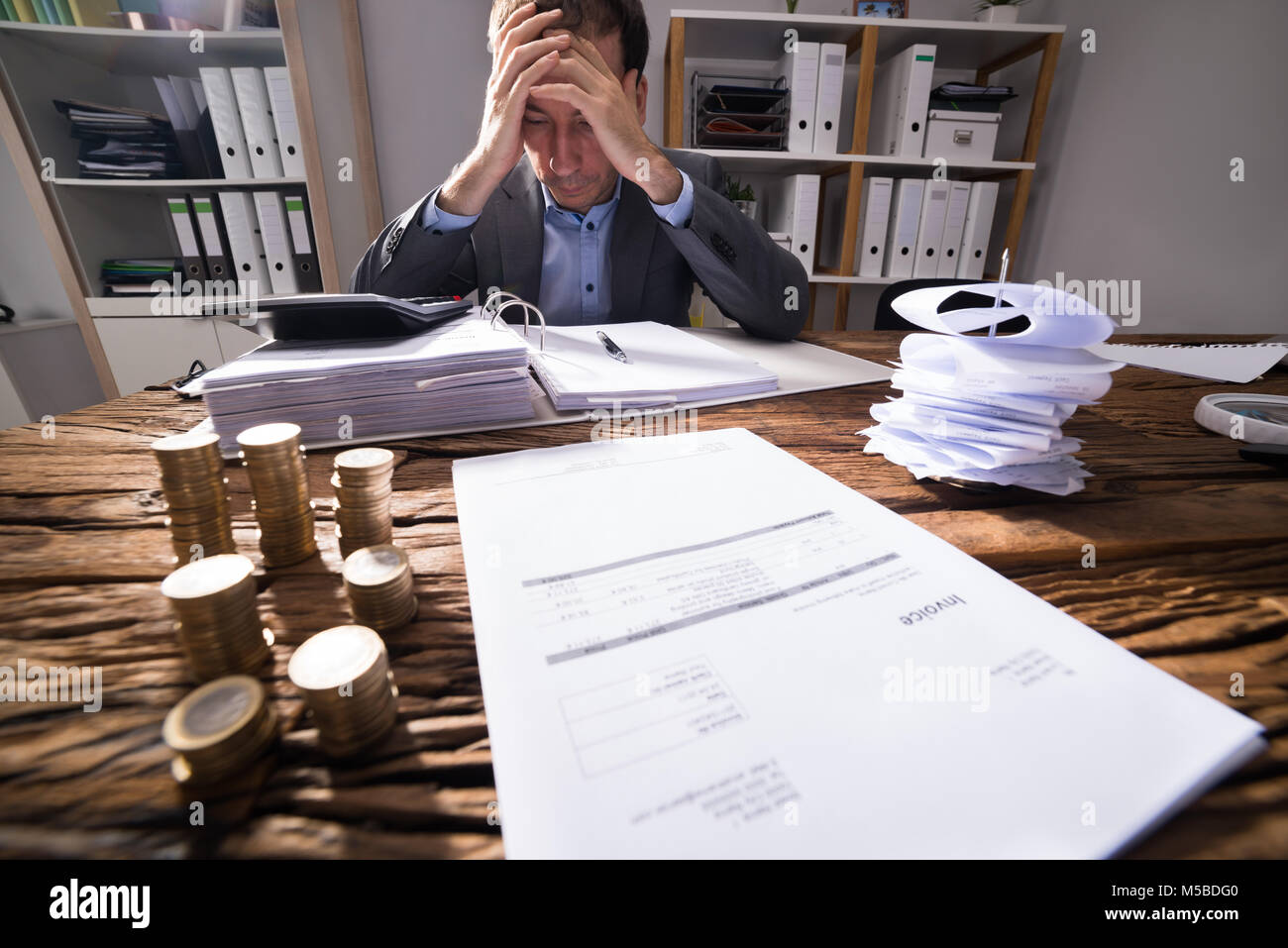 Stressed Businessman working in office avec facture et des pièces d'or empilés sur un bureau en bois Banque D'Images