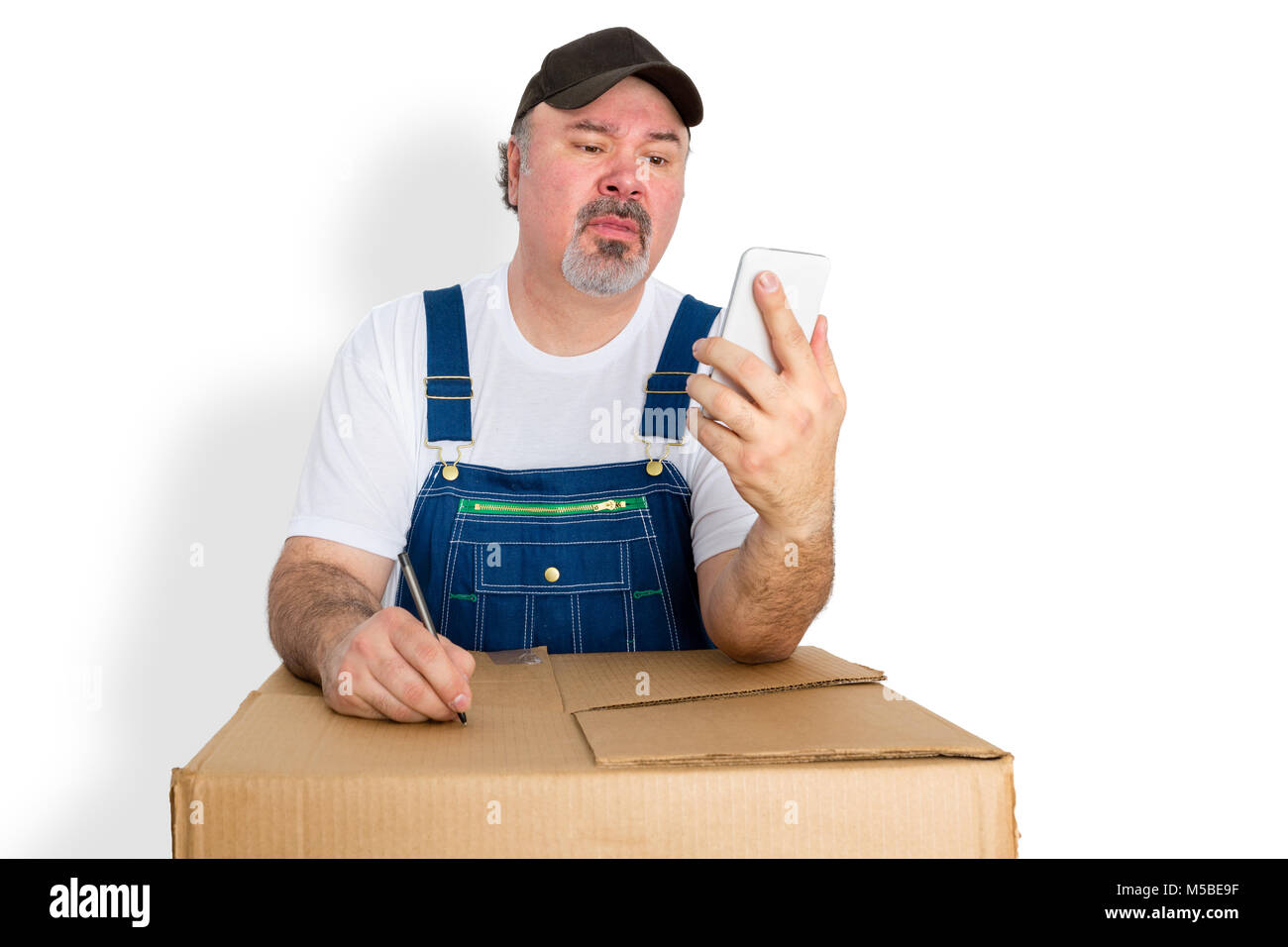 Livreur de mettre par écrit les instructions de son téléphone portable vers le couvercle d'une boîte en carton comme il se tient la lecture du message texte Banque D'Images